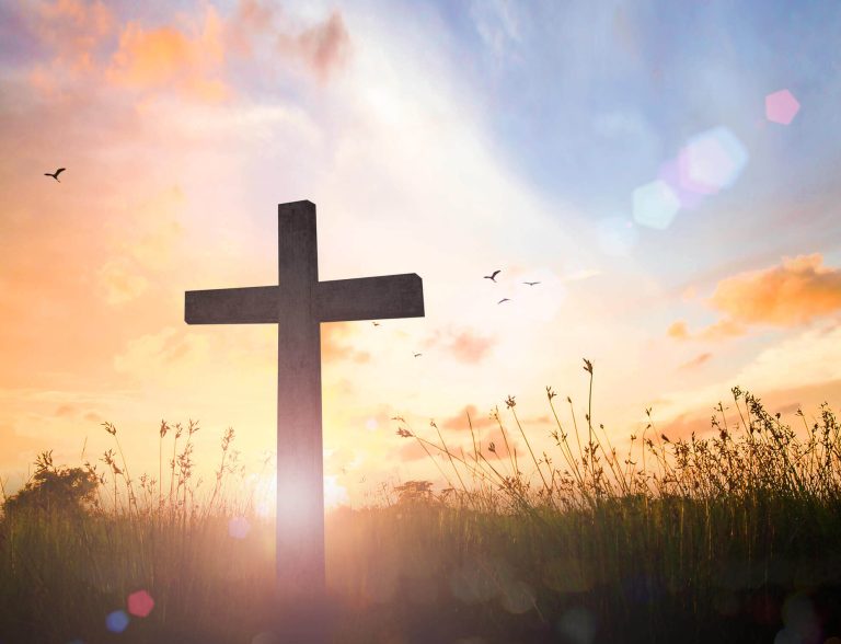 Christian Cross Silhouette at Sunrise with Light Rays and Peaceful Nature Landscape. Silhouette of a Christian cross standing on a grassy field during sunrise with warm sunlight and soft sky colors. The peaceful scene symbolizes faith, hope, spirituality, prayer, and the message of salvation in Christianity. Ideal concept for themes of worship, devotion, Easter reflection, and spiritual inspiration.