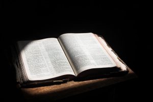 Open bible lying on a table. Old open bible lying on a wooden table in a beam of sunlight