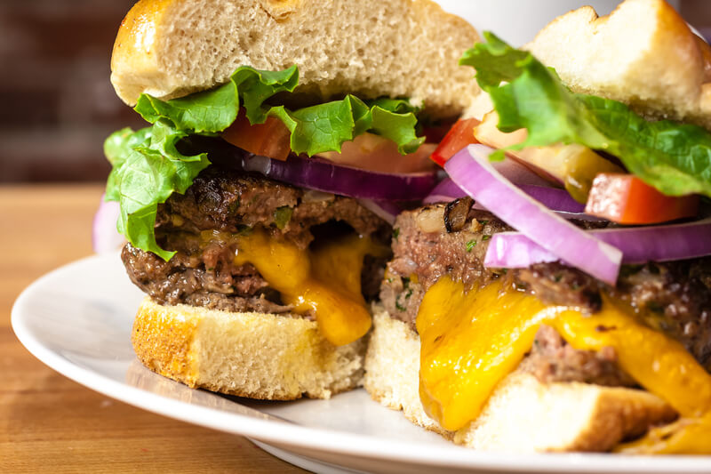 Close up of gourmet cheeseburger with melted cheese, tomatoes, lettuce and onions sitting on white plate