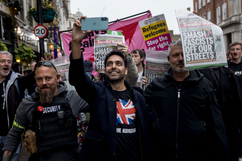LONDON, ENGLAND - OCTOBER 26: Right-wing internet personality Mahyar Tousi is led away by security as protesters from an anti-fascist demonstration chant and wave newspapers at him on October 26, 2024 in London, England. A protest organised by Tommy Robinson under the name Uniting the Kingdom and a counter-protest organised by Stand Up To Racism takes place in central London today. Robinson was held in custody yesterday afternoon and will miss the protest. (Photo by Jack Taylor/Getty Images)
