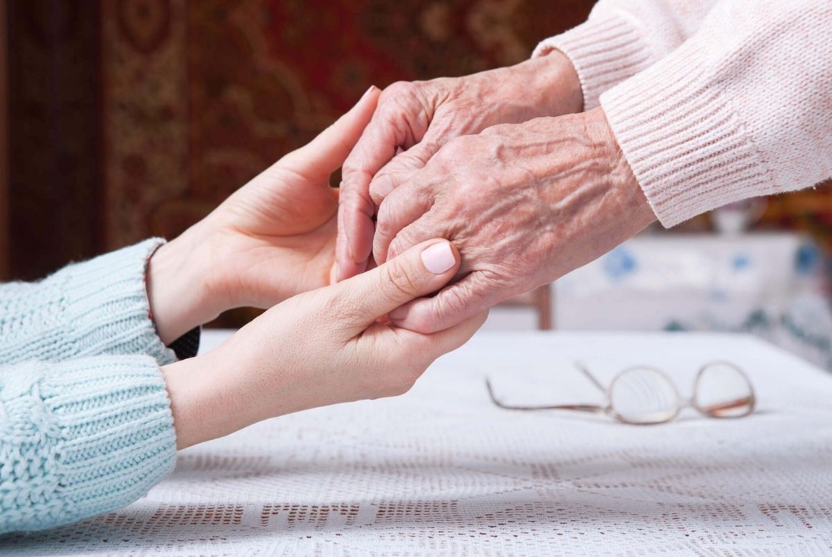 Care is at home of elderly. Senior woman with their caregiver at home. Concept of health care for elderly old people, disabled. Elderly woman holding hands closeup. Space for text white background.