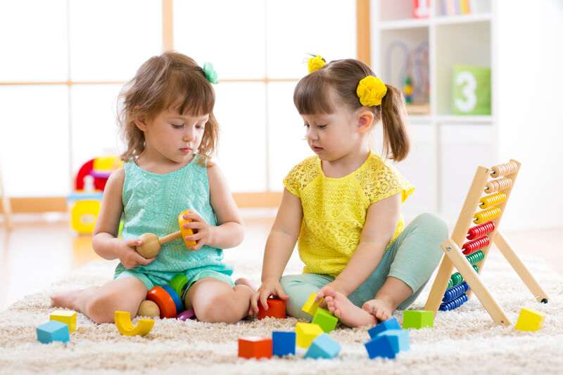 Children playing together with building blocks. Educational toys for preschool and kindergarten kids. Little girls build pyramid toys at home or daycare.