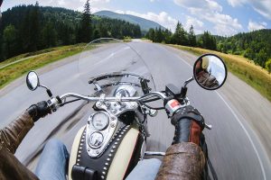 A first-person perspective of a person riding a motorcycle along an open road surrounded by a forest.