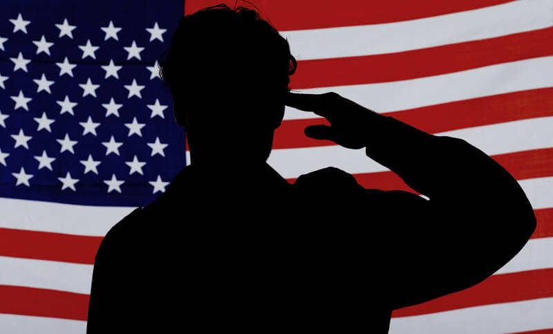 Silhouette of a soldier saluting against an American flag.