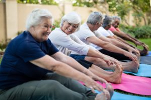 Cheerful senior women with friends doing stretching exercise at park