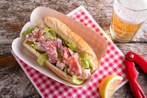 A delicious lobster roll with beer on a rustic wood table.