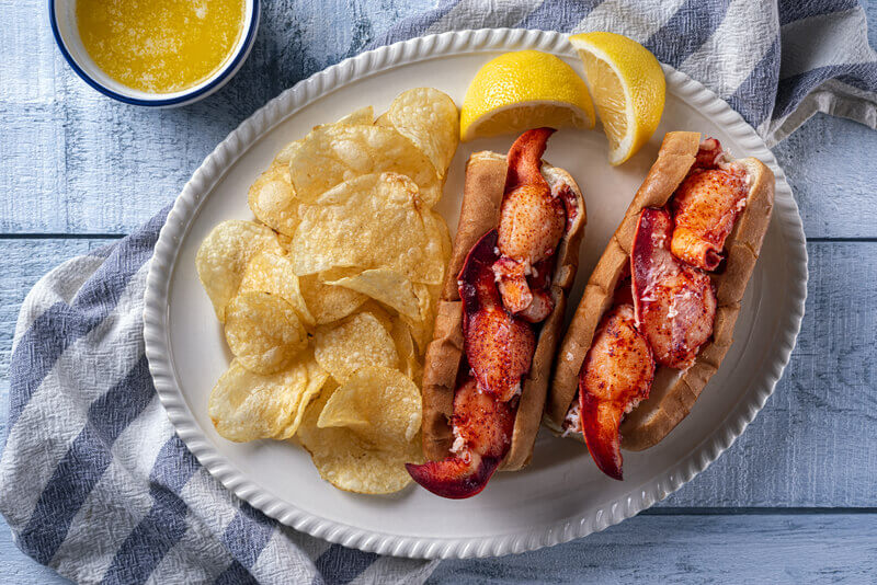 New England Lobster Rolls. Delicious New England style lobster rolls with potato chips and melted butter on a wood table top