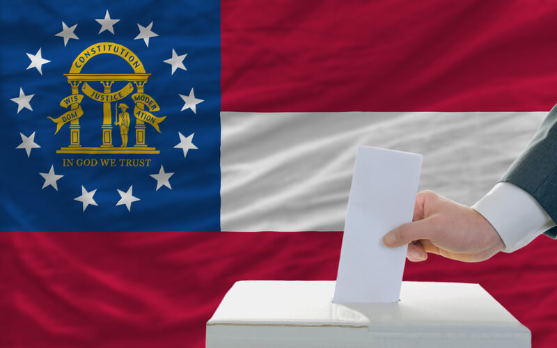 Man voting on elections in georgia. Man putting ballot in a box during elections in georgia in fornt of flag