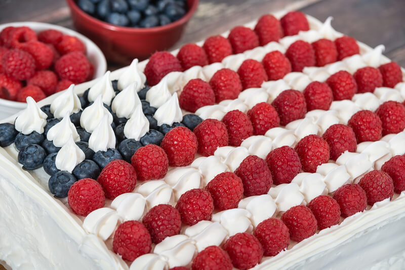Red white and blue American flag cake. Patriotic, red white and blue, American flag cake. Fresh blueberries and raspberries in the background. Concept for Fourth of July celebration.