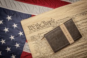 Holy bible on constitution and American Flag. A holy bible and crucifix rest atop the United States Constitution and American flag, which is emblematic of freedom of religion without persecution