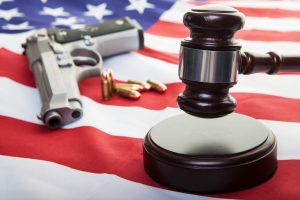 American Gun Law. A gavel on an american flag with a gun and bullets in the background, focus on the gavel.