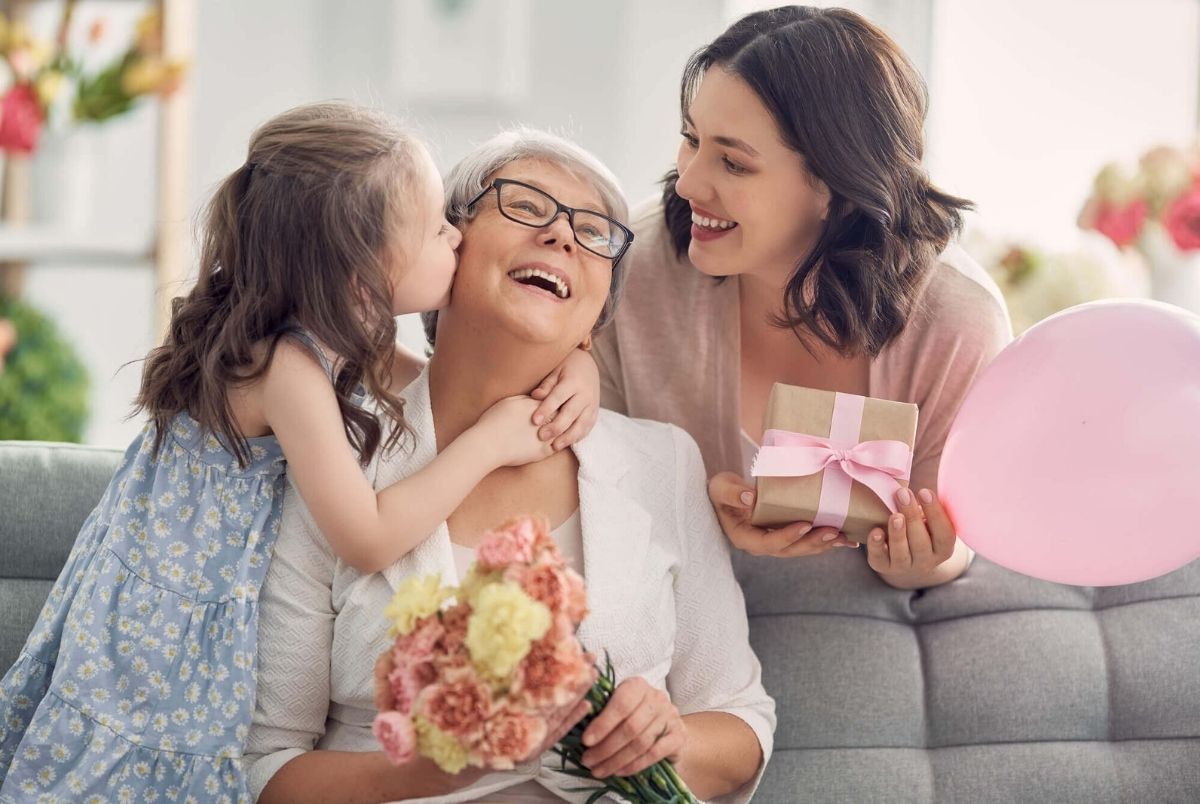 Happy mother`s day! Child daughter is congratulating mom and granny giving them flowers and gift. Grandma, mum and girl smiling and hugging. Family holiday and togetherness