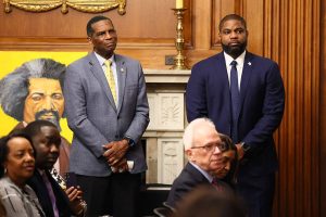 Rep. Burgess Owens (R-UT) and Rep. Byron Donalds (R-FL) listen as House Speaker Mike Johnson (R-LA) speaks in the Rayburn Reception Room after formally unveiling the Frederick Douglass Press Gallery in the US Capitol on February 12, 2026 in Washington, DC.