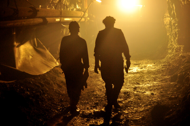 Two miners heading out from underground after their shift ends, in silhouette.