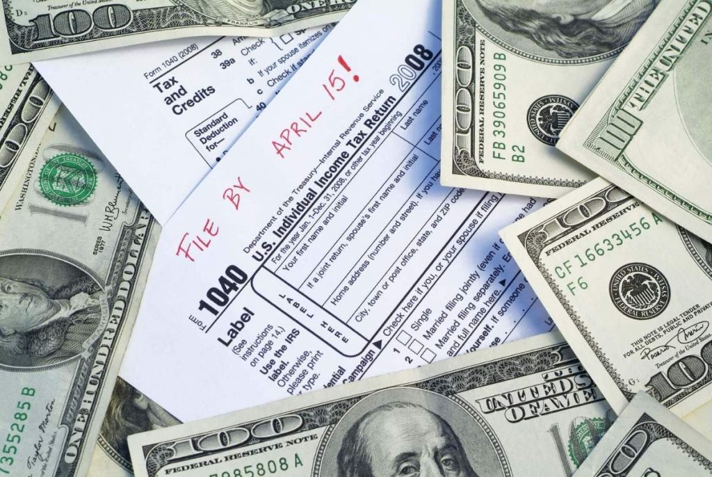 Taxes paperwork deadline. Blank 1040 US Tax Form with file by april 15th written on the top, and surrounded by one hundred dollar American government currency. 4
