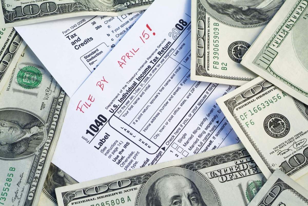 Taxes paperwork deadline. Blank 1040 US Tax Form with file by april 15th written on the top, and surrounded by one hundred dollar American government currency. 4