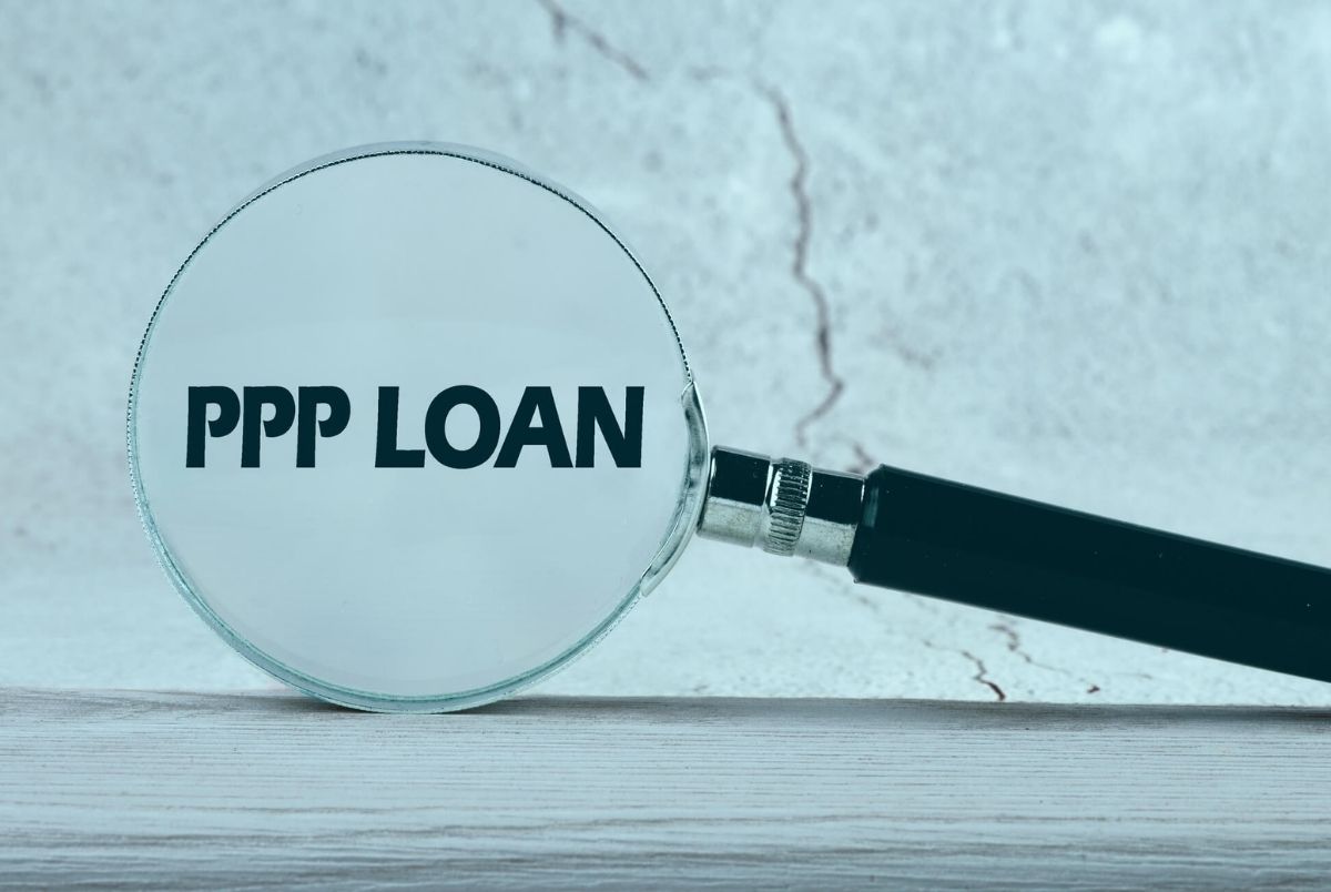 Paycheck Protection Program PPP Loan written through a magnifying glass on a gray background.