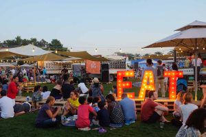 A large outdoor festival featuring food trucks, live music, and string lights, which resembles events like the Food Truck Jam in Dubai.
