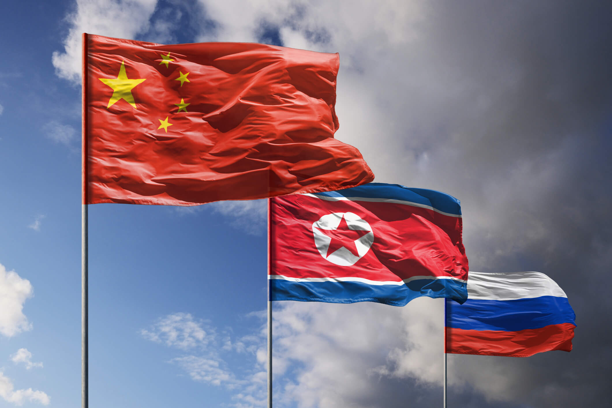 Flags of China, North Korea and Russia above dark sky