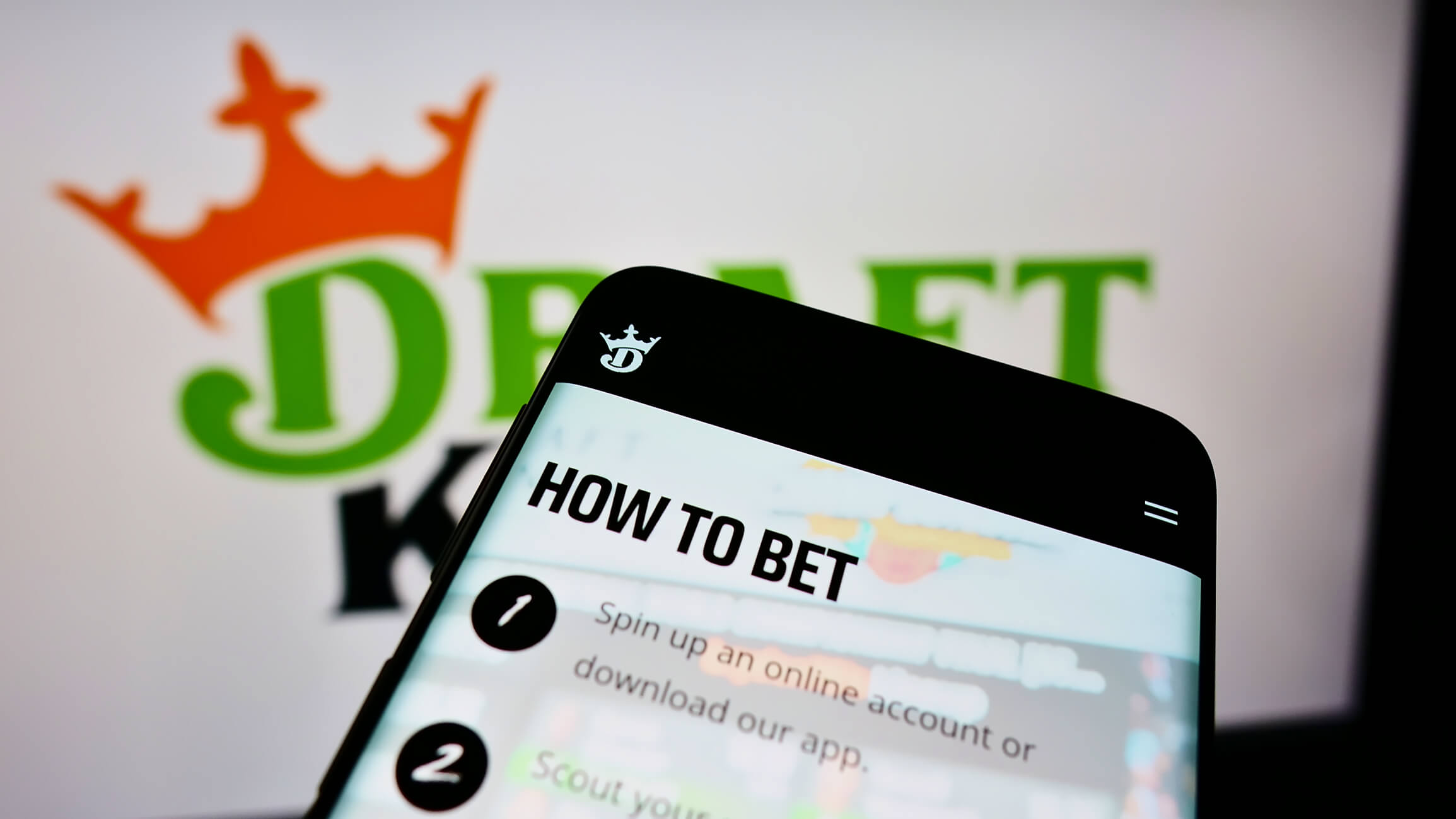 Mobile phone with website of American sports betting company DraftKings Inc. on screen in front of logo. Focus on top-left of phone display.