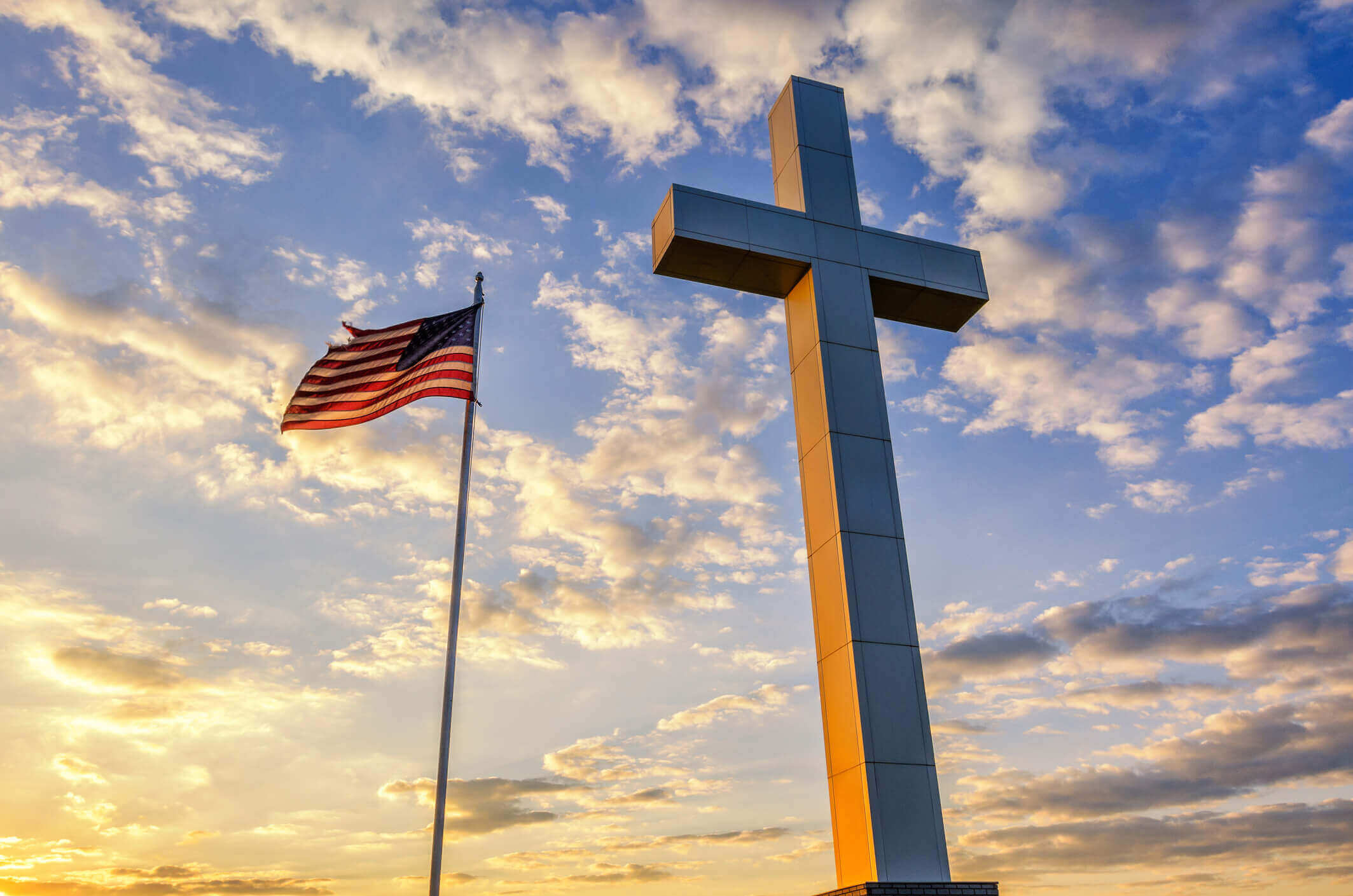 Cross and American Flag at sunset. A worn American Flag flies next to this Cross monument at sunset in Western Kentucky near the convergence of the Ohio and Mississippi Rivers.
