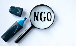 NGO - acronym under a magnifying glass with a marker on a white background. NGO (Non-governmental organization) - acronym under a magnifying glass with a marker on a white background