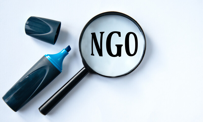 NGO - acronym under a magnifying glass with a marker on a white background. NGO (Non-governmental organization) - acronym under a magnifying glass with a marker on a white background