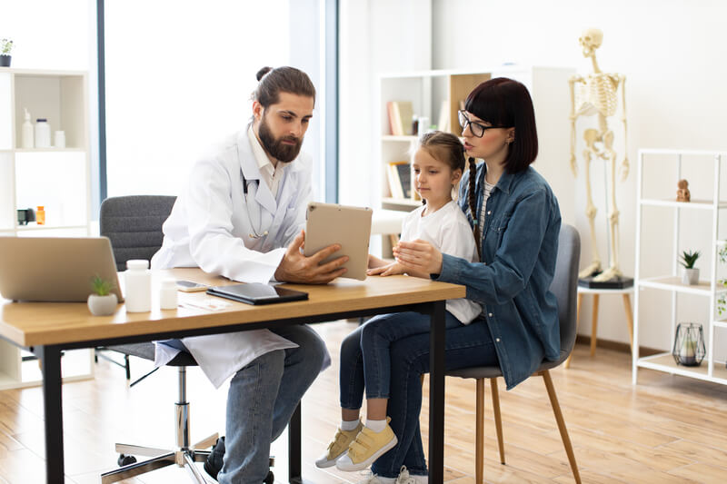 Doctor presenting medical results to concerned mother and sick child. Caucasian doctor shows test results and treatment prescription to little sick girl and mother in clinic. Scene depicts professional healthcare, caring communication, and supportive environment.
