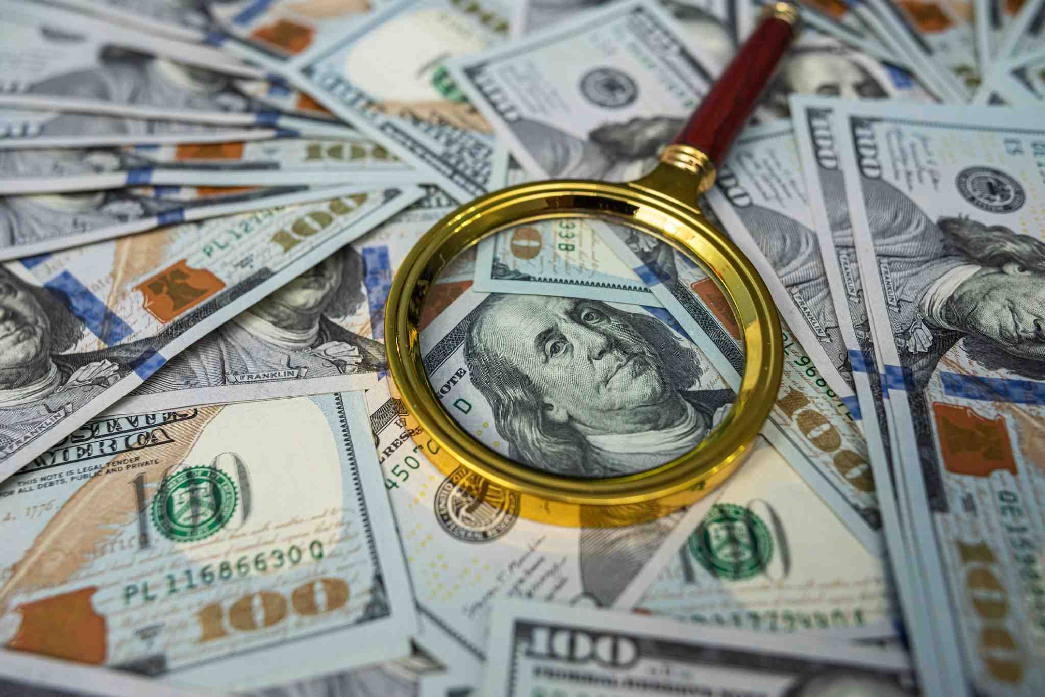 Close-up of a golden magnifying glass inspecting US dollar banknotes.