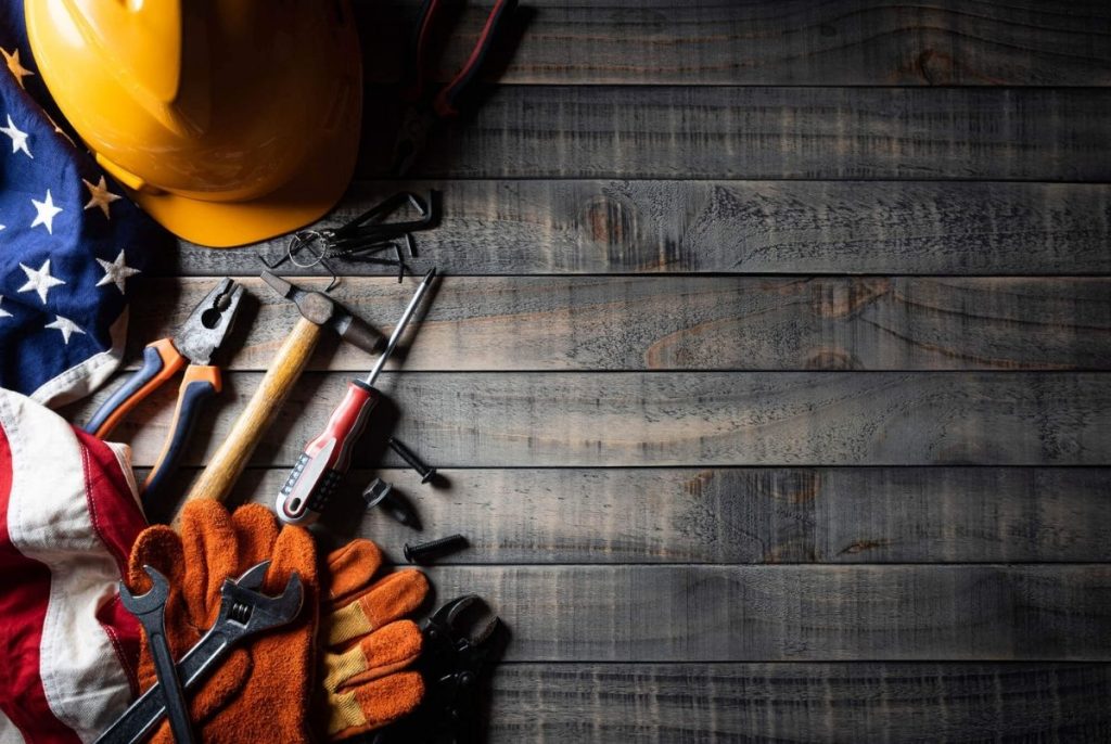 Happy Labor day concept. American flag with different construction tools on dark wooden background, with copy space for text.