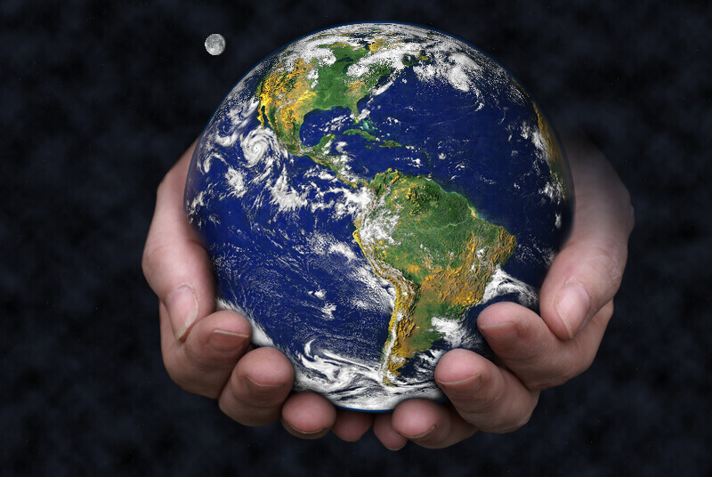 A pair of hands holding the Earth with the moon in the background. Blue Marble picture courtesy of NASA, see for terms of use