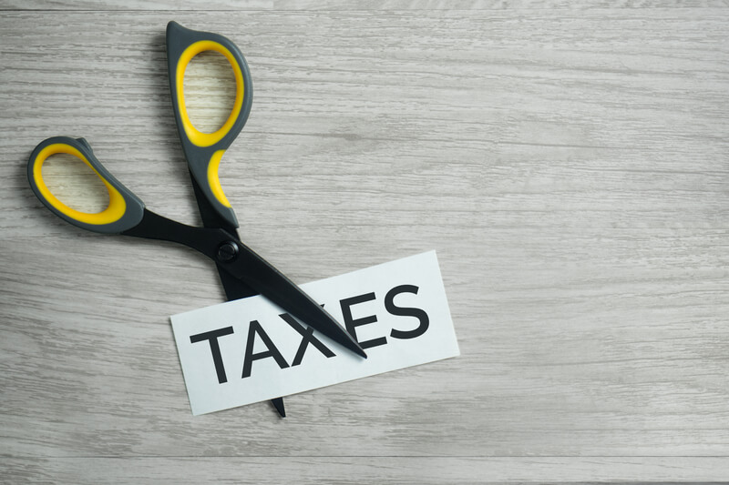 Scissor Cutting the Word Taxes. Scissor cutting `Taxes` word on wood background.