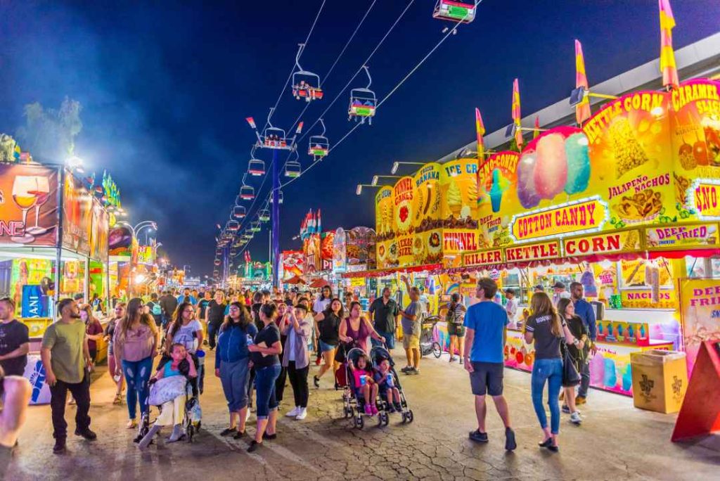The Arizona State Fair in Phoenix, featuring a bustling midway with colorful concession stands and a sky lift ride overhead.