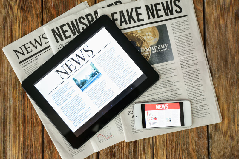 Newspapers, tablet computer and phone with news on screen on wooden table