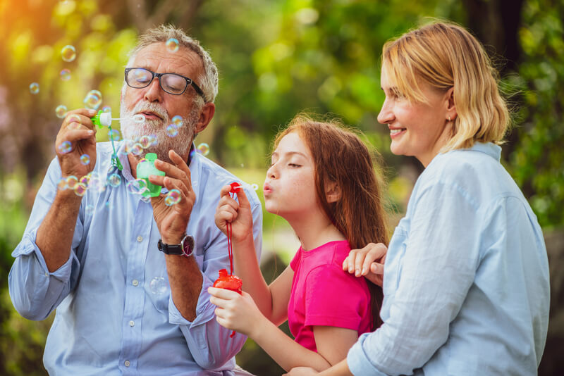 Happy family blowing soap bubbles in the park. Happy family blows soap bubbles together while going vacation on weekend in the garden park in summer. Kid education and family activities concept.