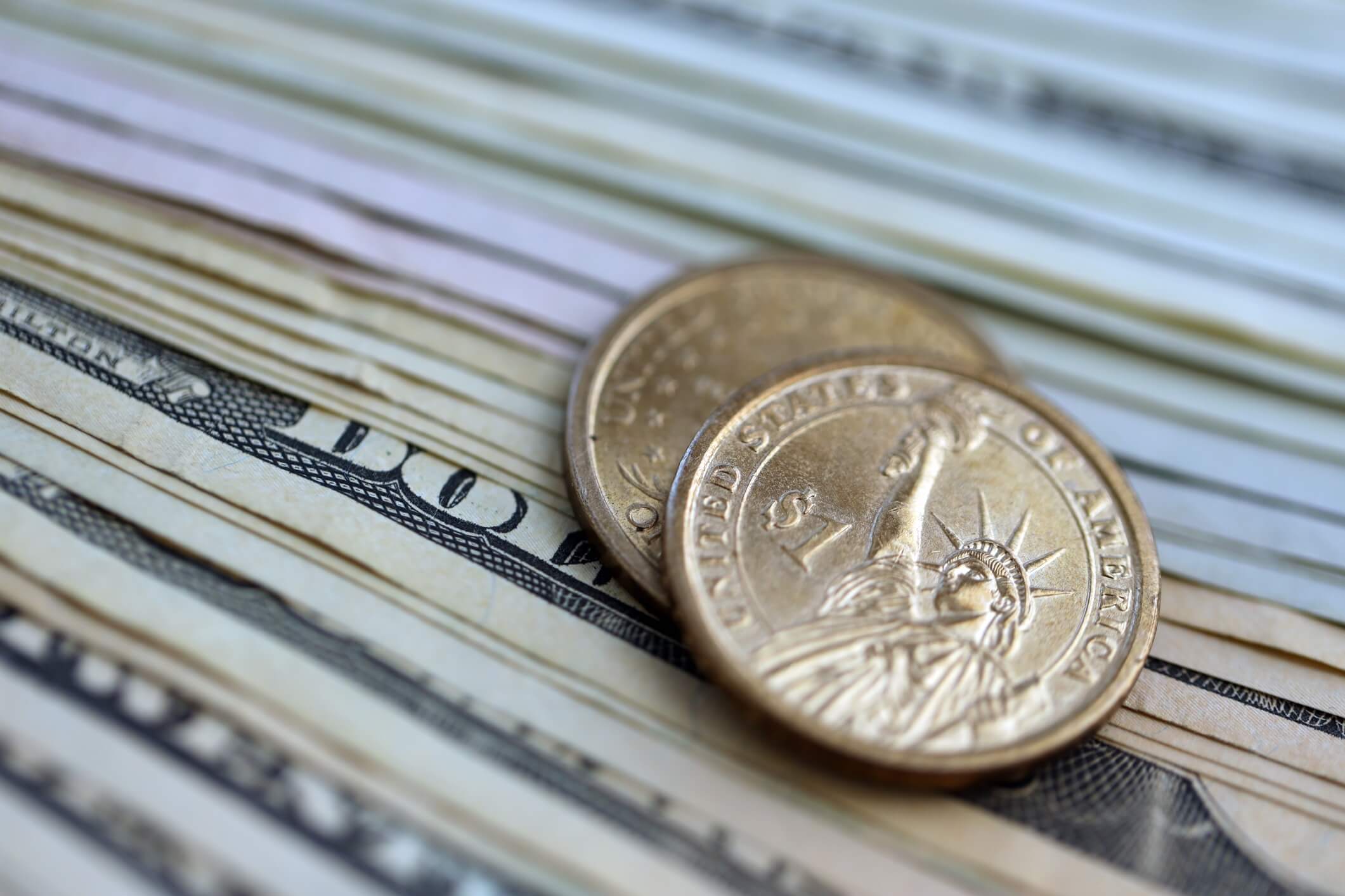US dollar money bills and two dollar coins pile. United States coins on banknotes of USD currency. Concept of business, taxes and banking in United States.